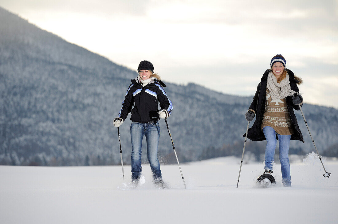 Two young women walking with snow shoe on snow covered meadow, valley of Leitzachtal, Upper Bavaria, Bavaria, Germany, Europe