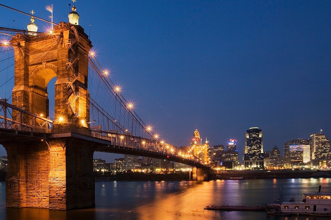 Cincinnati Ohio skyline as seen from Covington Kentucky across the Ohio River at night with the the John A Roebling Suspension Bridge