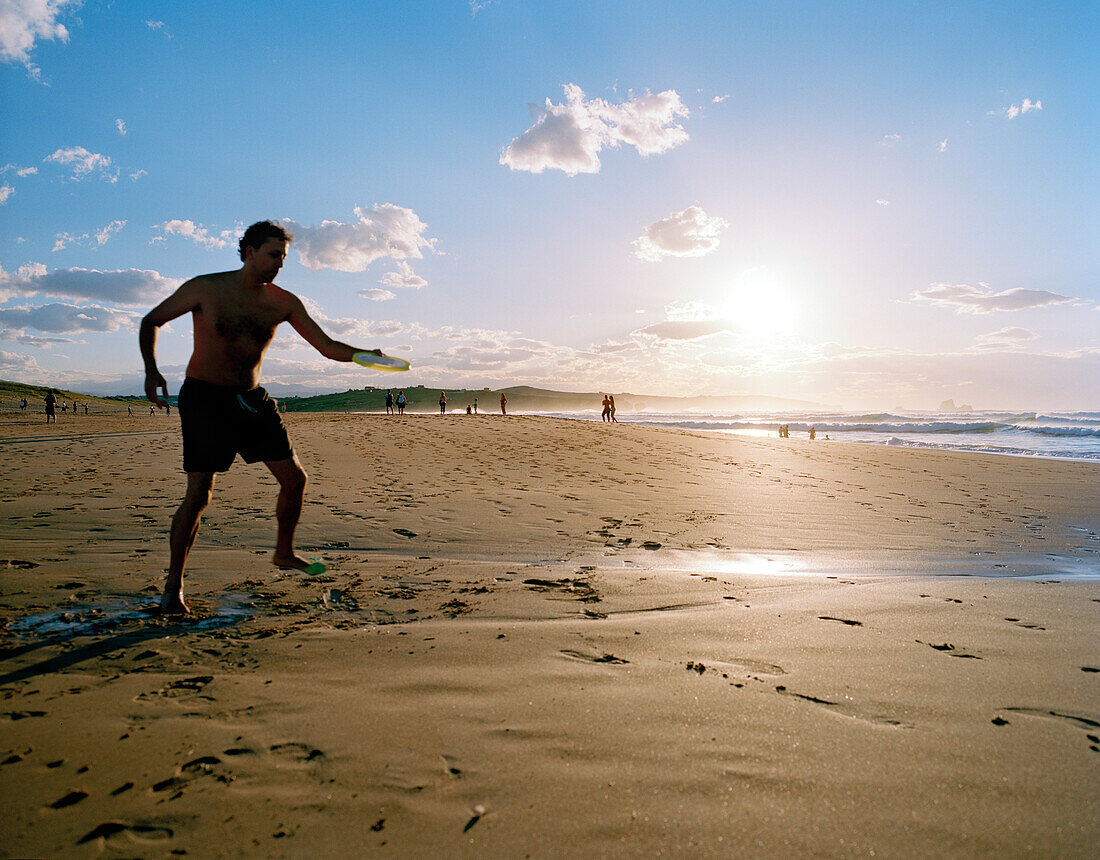 Frisbeespieler bei Sonnenuntergang am Strand, Playa de Valdearenas, westlich Santander, Kantabrien, Spanien