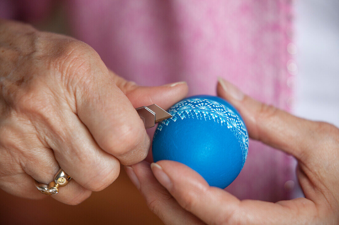 Senior woman scratching patterns on a blue easter egg, Easter, Spring