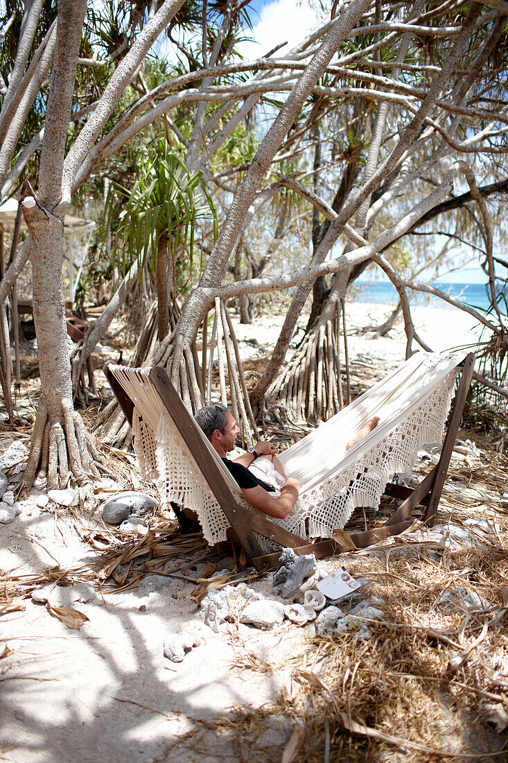 Guest in the hammock right at the beach under Pandanus trees, Wilson Island Resort, Wilson Island, part of the Capricornia Cays National Park, Great Barrier Reef Marine Park, UNESCO World Heritage Site, Queensland, Australia