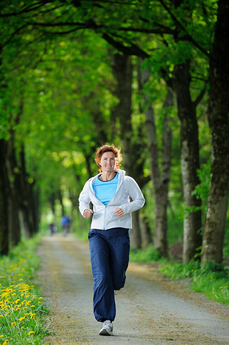 Frau läuft durch eine Allee, Oberbayern, Bayern, Deutschland