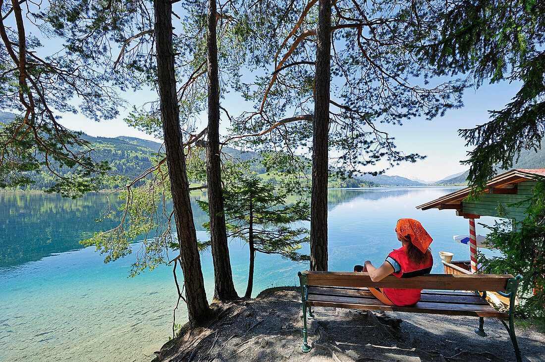 Frau sitzt auf Holzbank und genießt Aussicht über Weißensee, Weißensee, Kärnten, Österreich, Europa