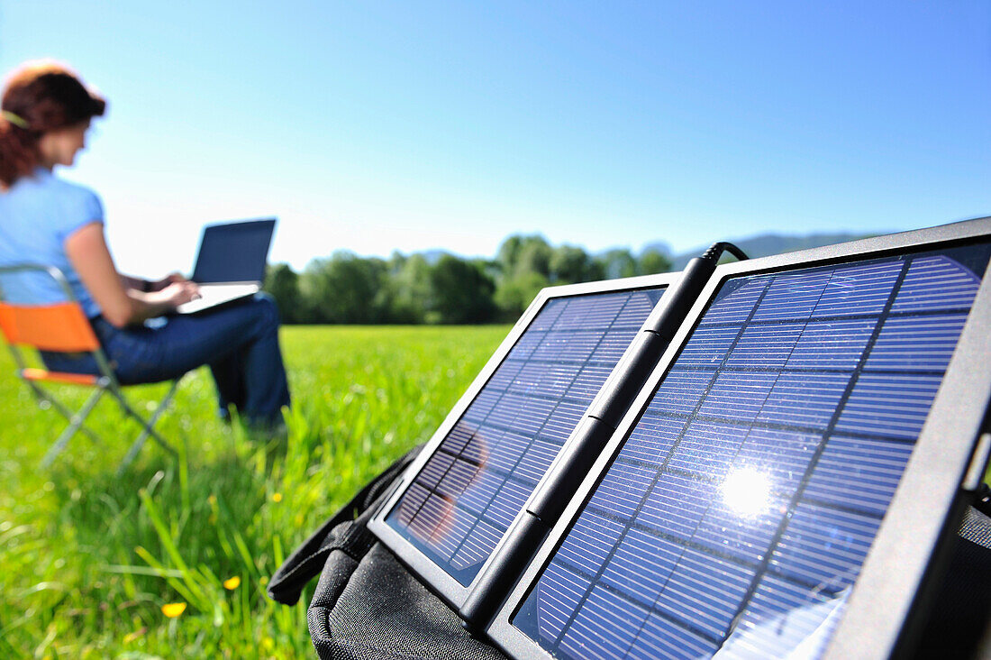 Frau sitzt auf einer Wiese und arbeitet an einem Laptop, Solarmodul im Vordergrund, Bayern, Deutschland