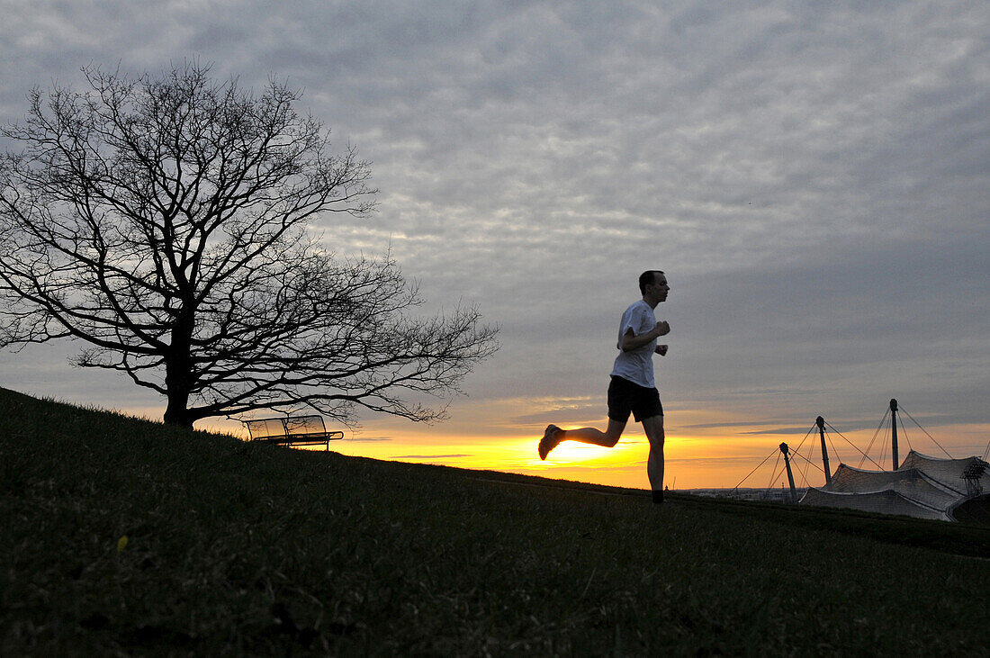 Mann beim Joggen, Sonnenuntergang im Olympiapark, München, Bayern, Deutschland