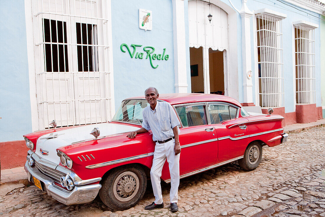 Man standing in front of his red vintage American car (Chevrolet) in front of Via Reale, Trinidad, Sancti Spiritus, Cuba