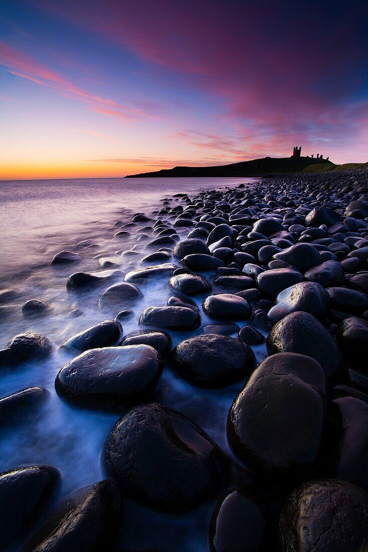 England, Northumberland, Embleton Bay Waves crash againt the sea scultured rocks dominating the coastline of Embleton Bay, overlooked by the dramatic ruins of Dunstanburgh Castle