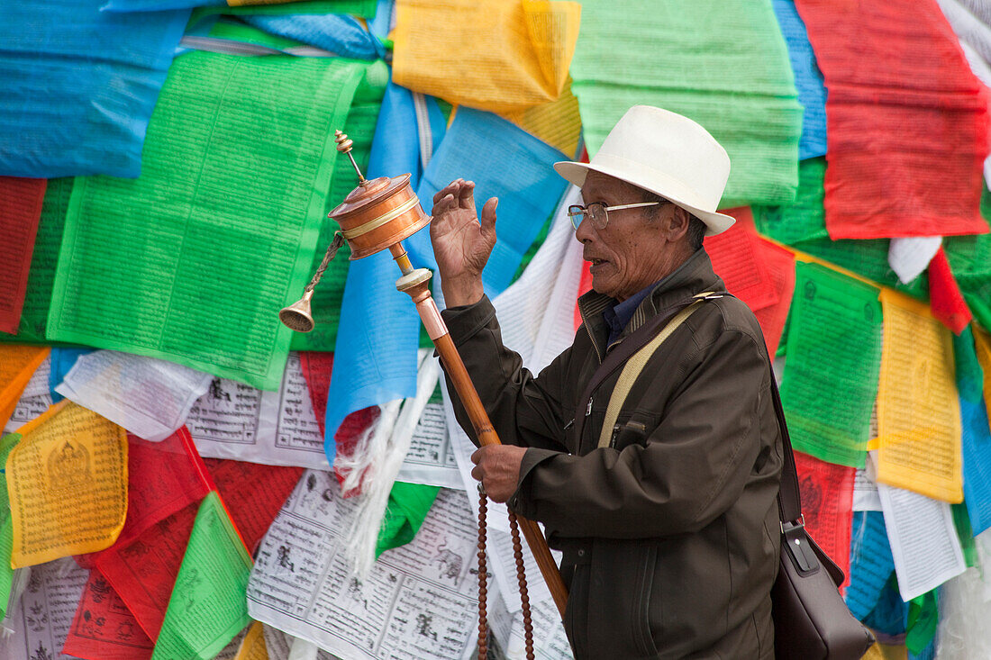 Buddhistic pilgrim with prayer wheel in front of prayer flags in, Tibet Autonomous Region, People's Republic of China