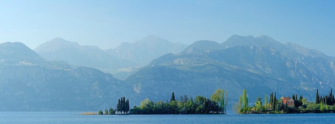 Island with cypresses in Lake Garda, mountain range in background, Veneto, Italy