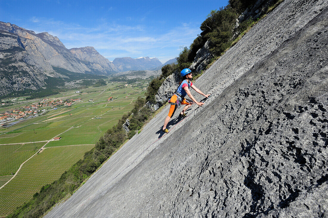 Frau klettert an einer Felswand, Sarcatal und Gardaseeberge im Hintergrund, Dro, Trentino, Italien, Europa