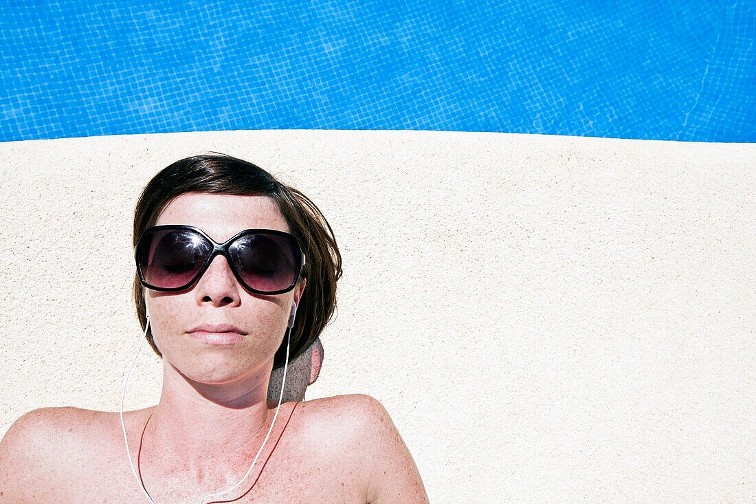 Shot of an Attractive Brown Haired Woman Next to the Pool with her Earphones