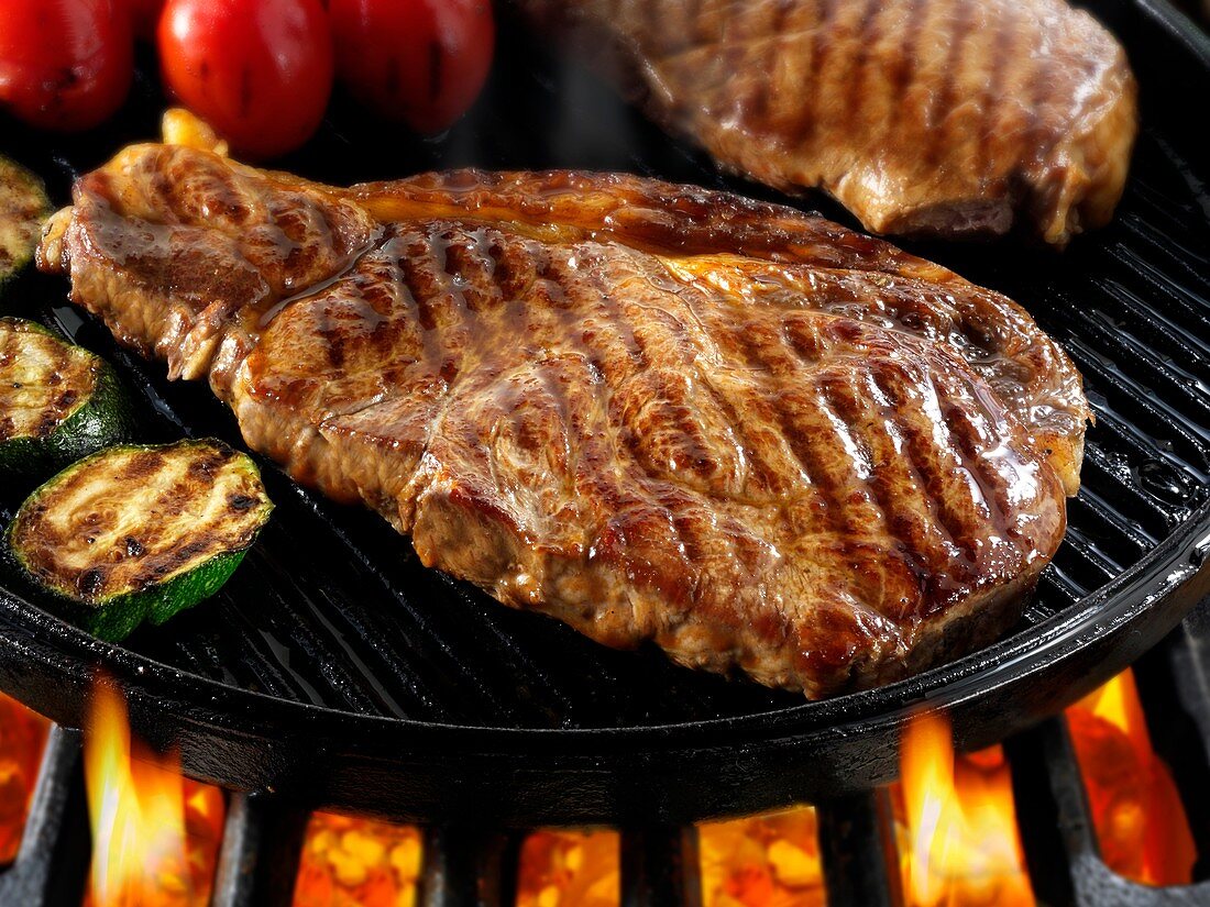 Sirloin beef steaks & tomatoes being pan fried on a bbq
