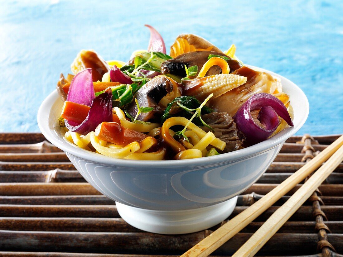 Oriental vegetarian stir fry of vegetables, noodle and mushrooms in a bowl with chop sticks