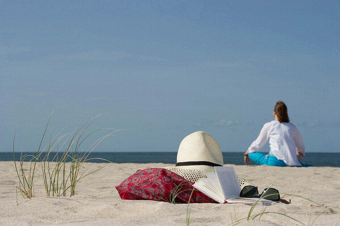 Frau sitzt am Strand, Buch und Sonnenbrille im Vordergrund, List, Sylt, Schleswig-Holstein, Deutschland