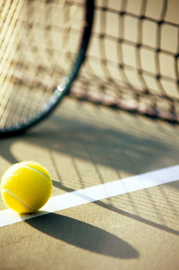 Tennis racket and ball next to net with shadows on court