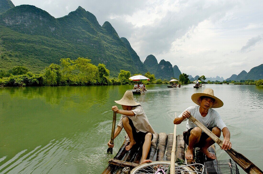 China guangxi yangshuo a chinese couple rowing on a bamboo raft on the yulong river with tourists on board