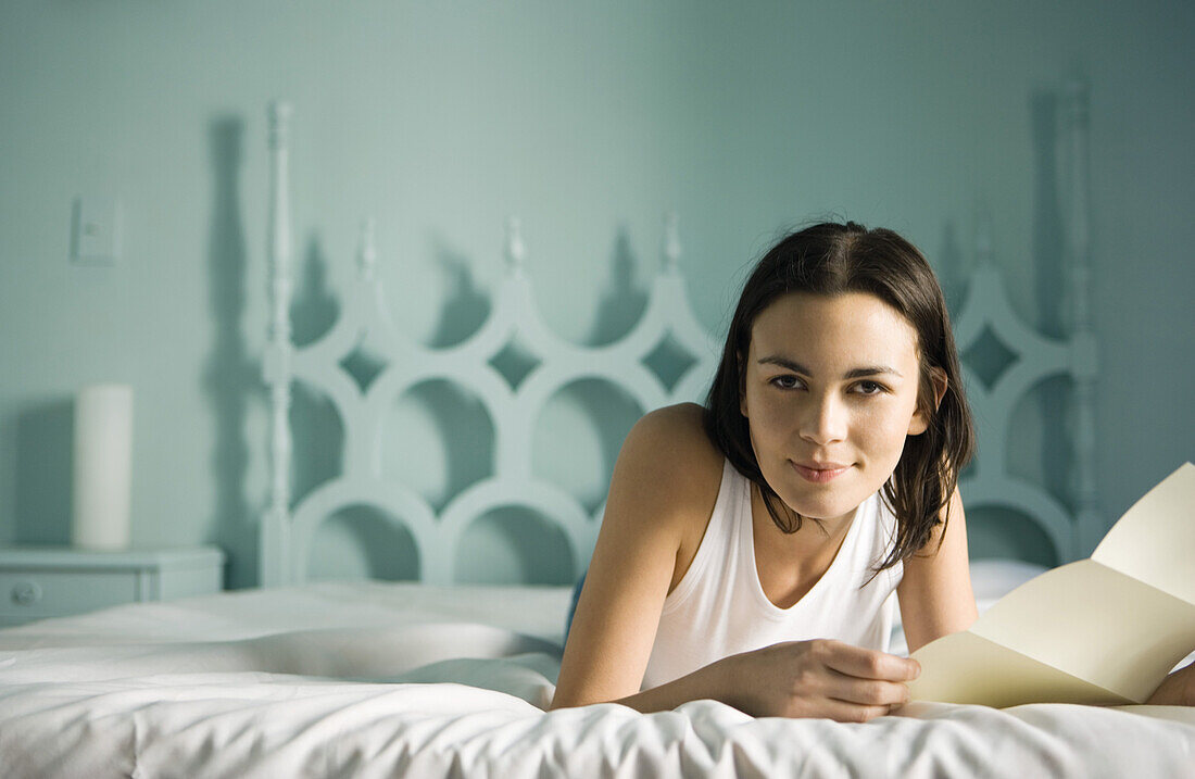 Woman lying on bed with letter, smiling at camera