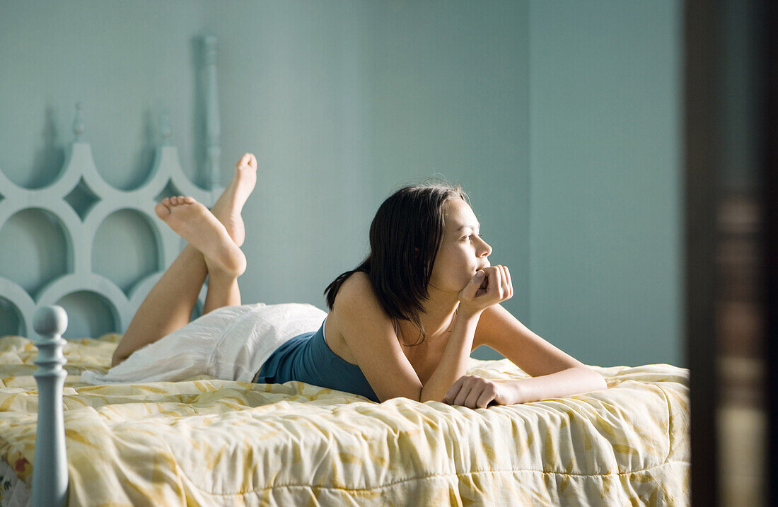 Woman lying on bed with hand under chin, legs up