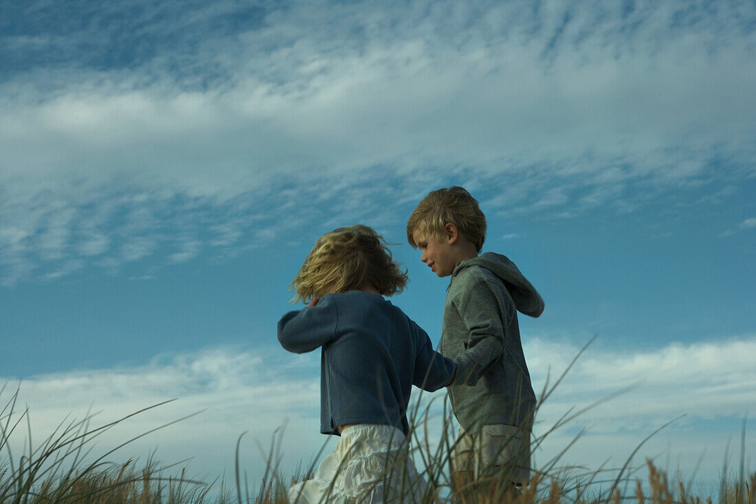 Boy and girl walking side by side through tall grass, holding hands