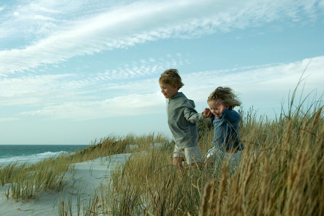 Boy and girl running through dune grass, holding hands