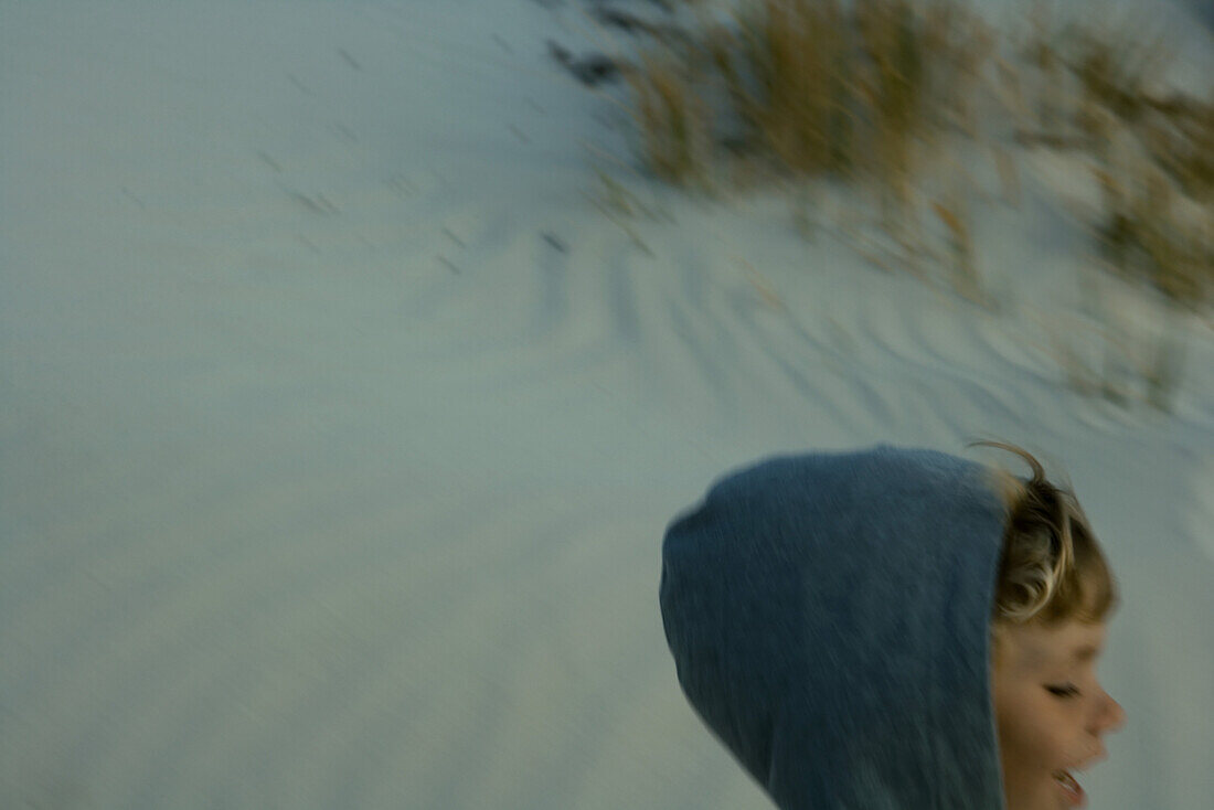 Child wearing hooded sweatshirt on dune, cropped