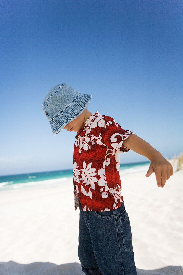 Boy standing on beach with arms out and head down