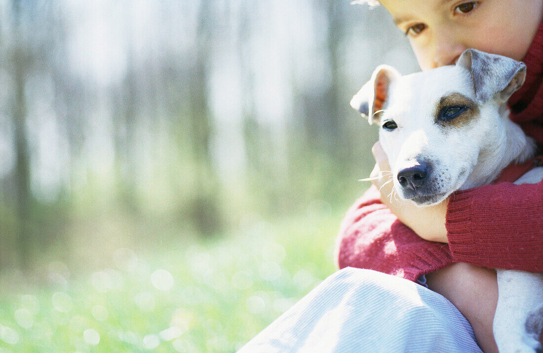 Child sitting on grass with dog in arms