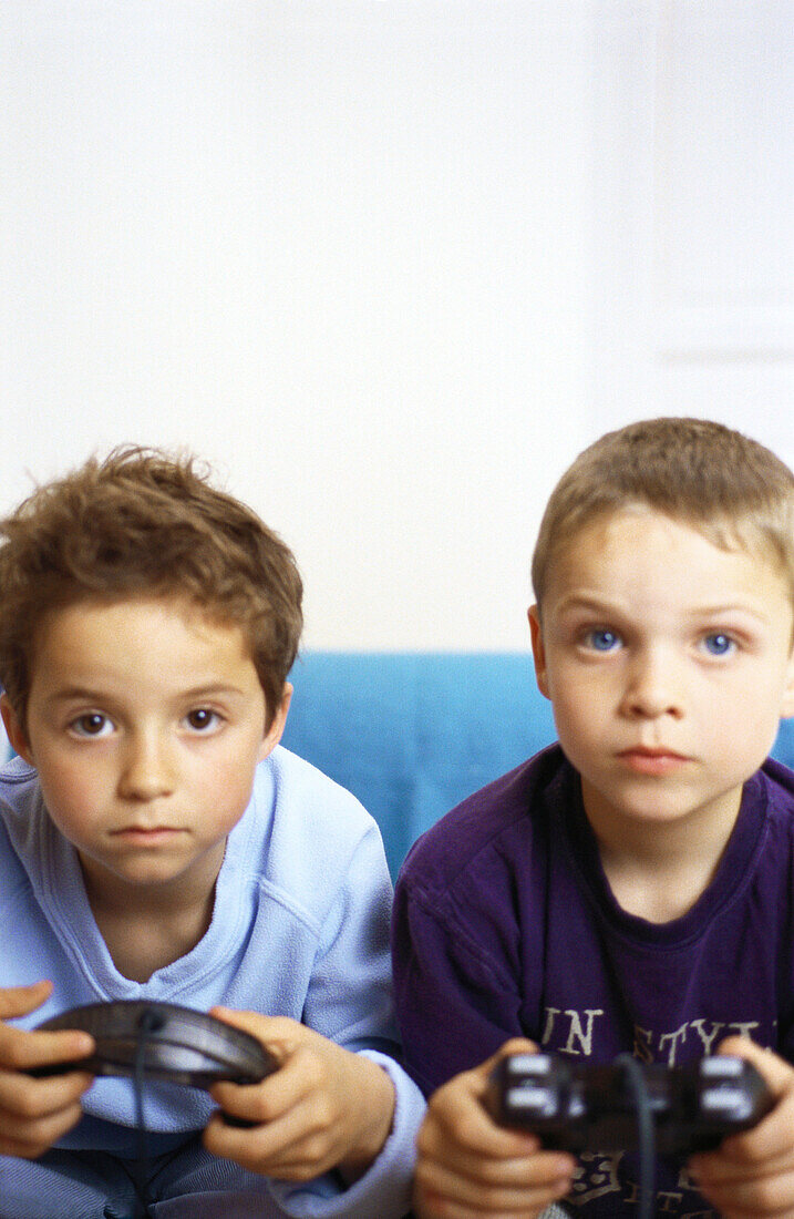 Two boys sitting on sofa holding joysticks
