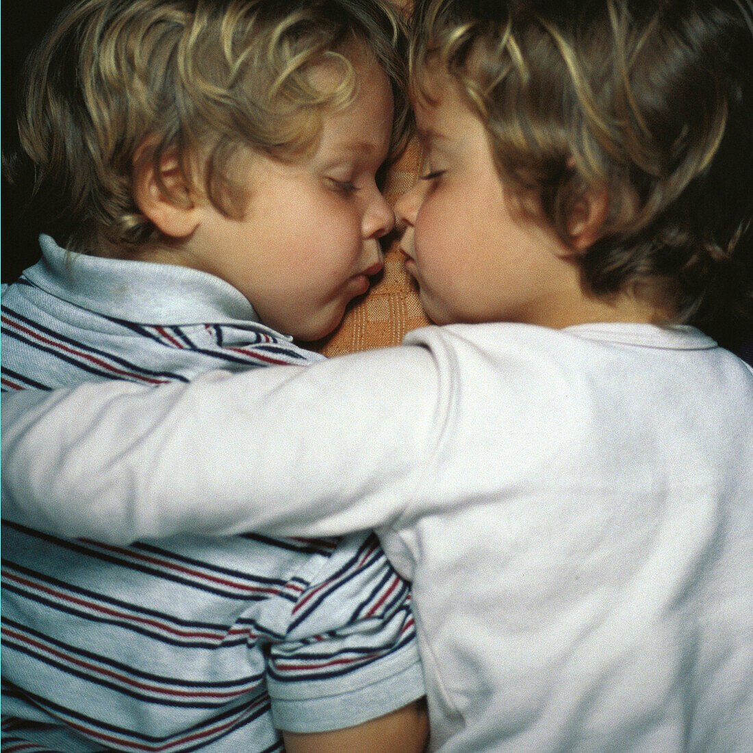 Two children sleeping, face to face, one with arm around the other