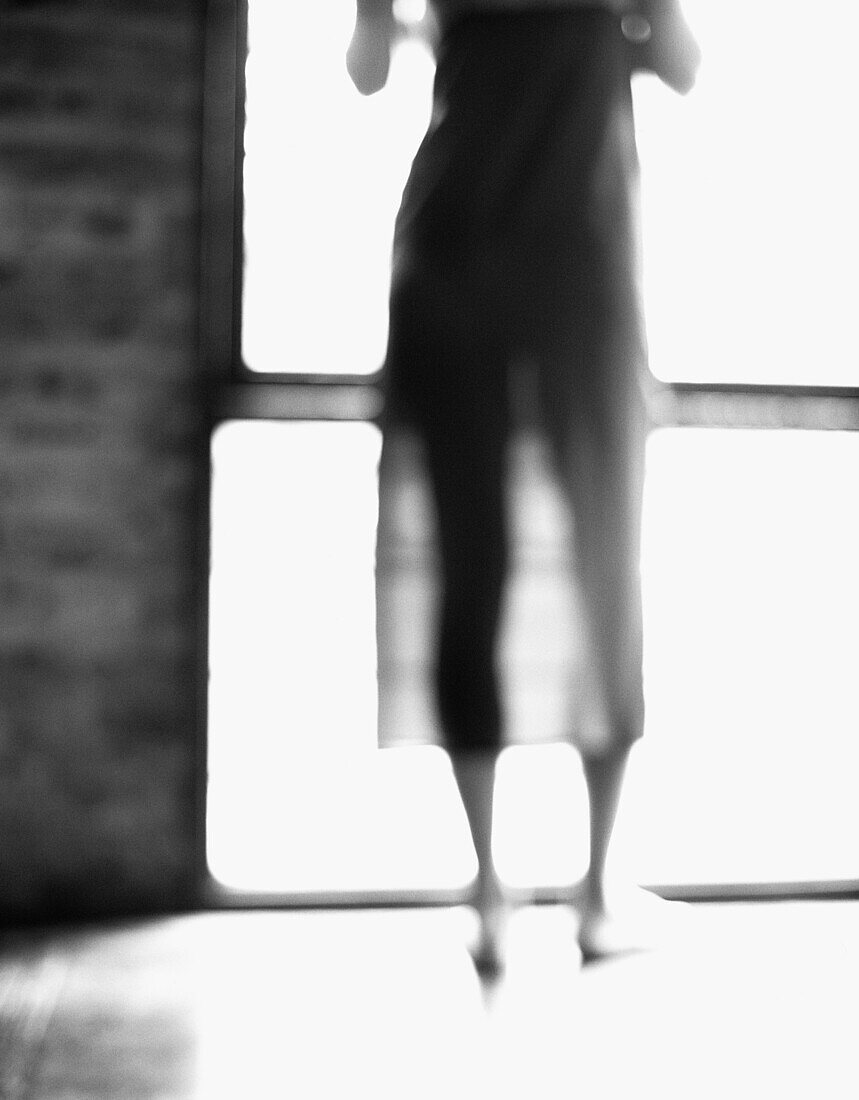 Young woman standing in front of window, chest down, rear view, b&w, defocused