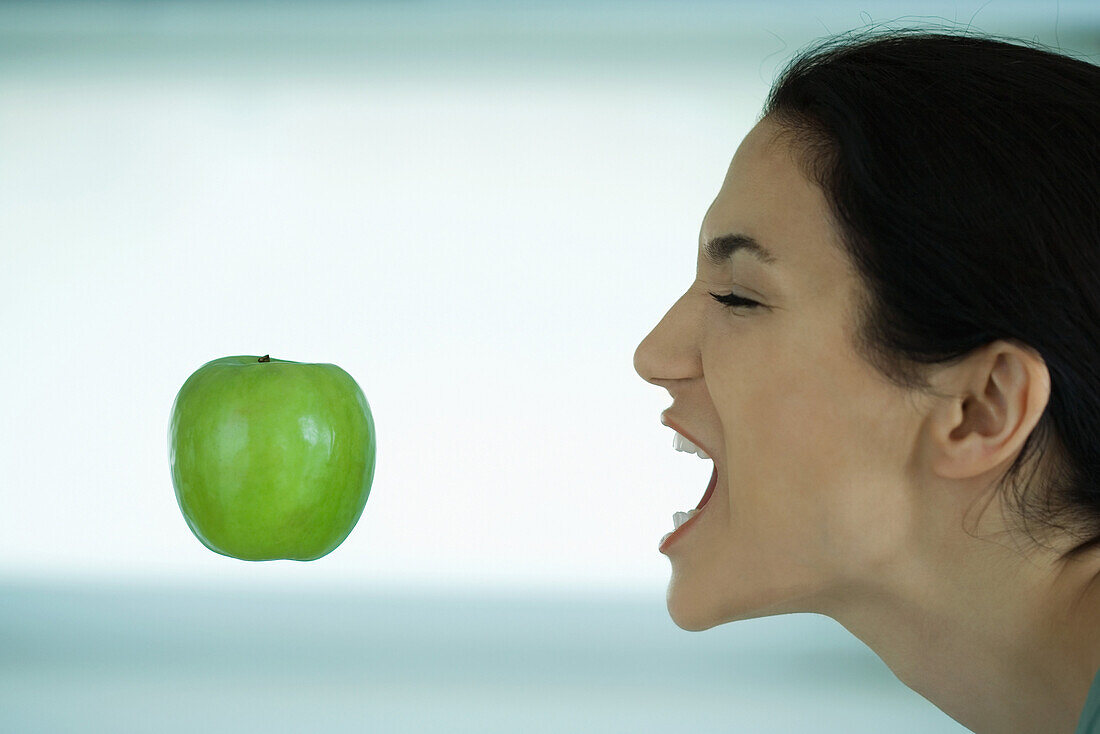 Apple floating in air, woman reaching for it with open mouth, eyes closed