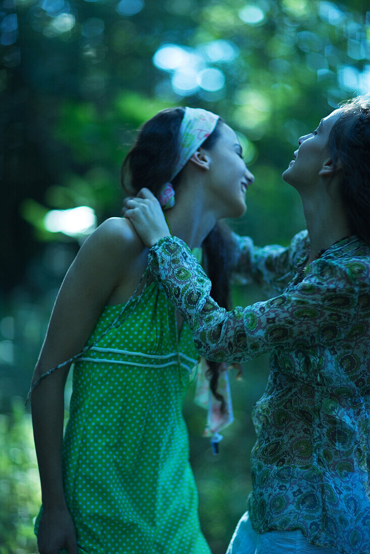 Zwei junge Frauen umarmen sich im Wald, schauen weg und lachen