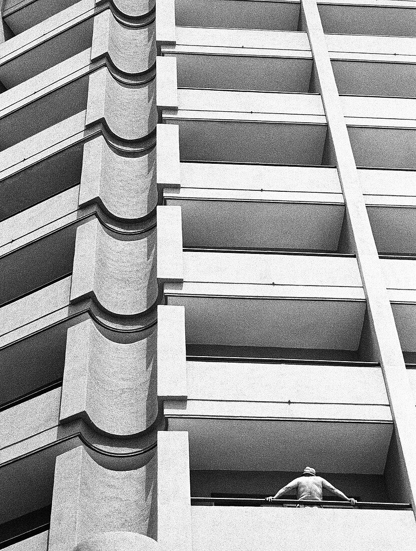 Facade of apartment building, person leaning against railing, b&w