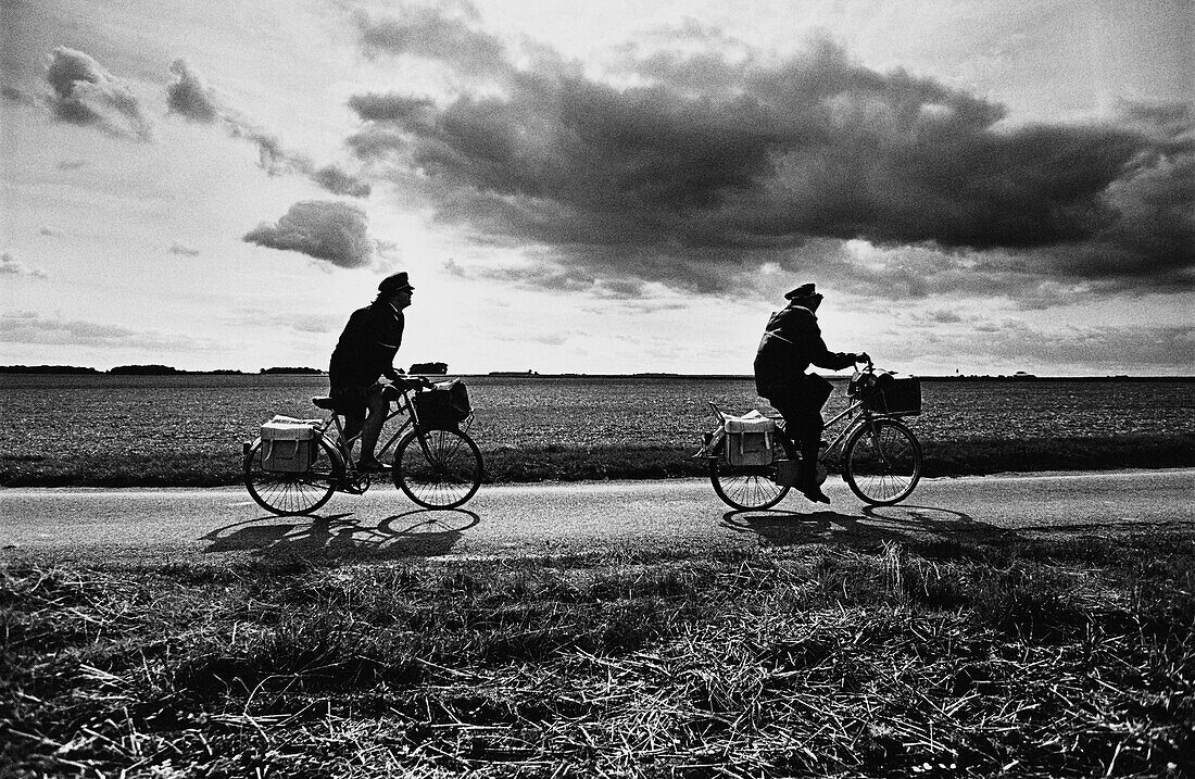 Two people on bicycles on road through fields, b&w