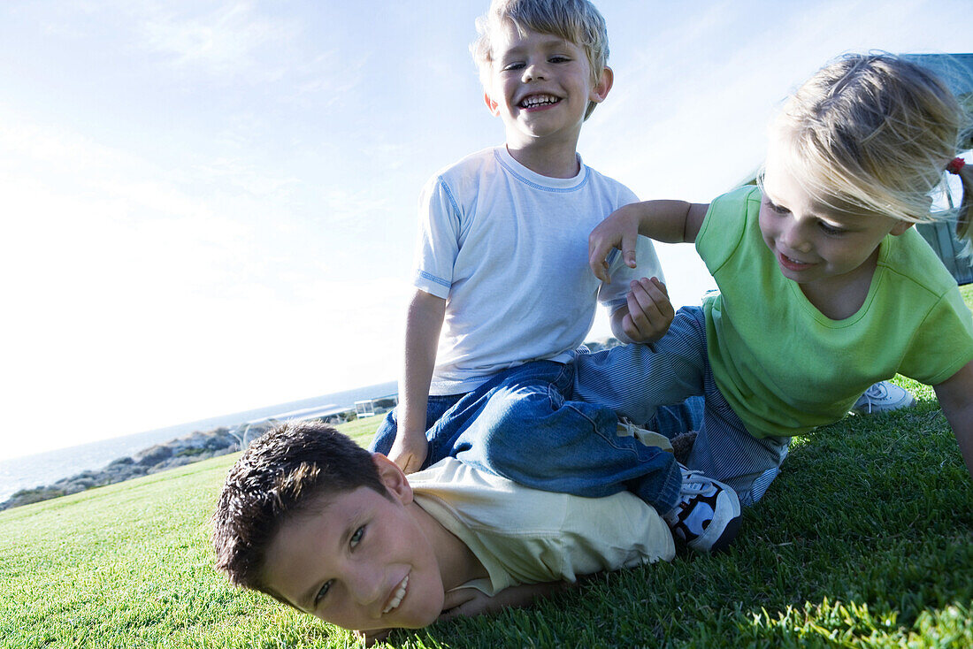 Three children wrestling on grass, smiling