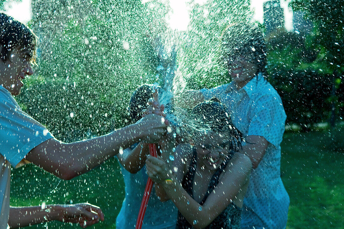 Young friends having water fight with garden hose