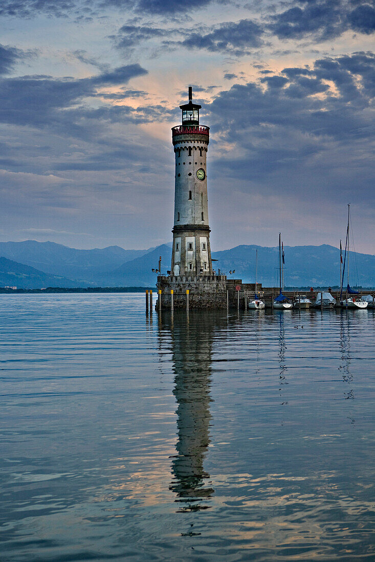 Old-fashioned ocean lighthouse on end of jetty with boats moored along side