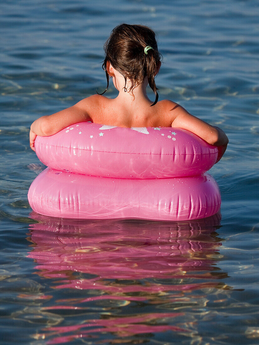 Young Girl Sitting in Pnk Floating Rings in Water, Rear View