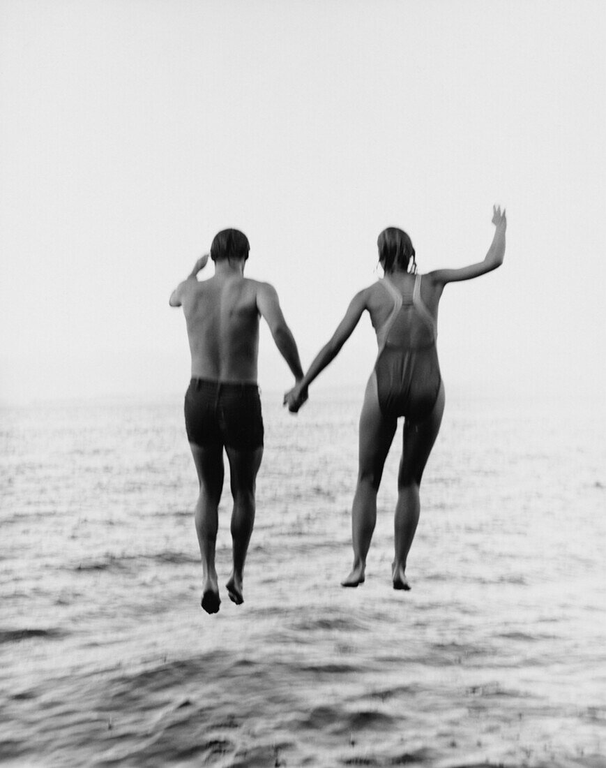 Couple Holding Hands While Jumping Into Water