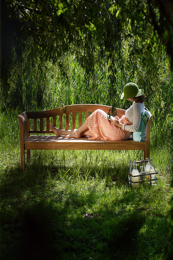 Young woman reading a book on a garden bench, Simssee, Bavaria, Germany