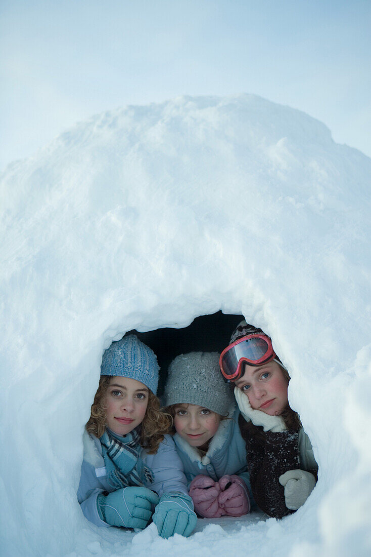 Three young friends lying in igloo, smiling at camera