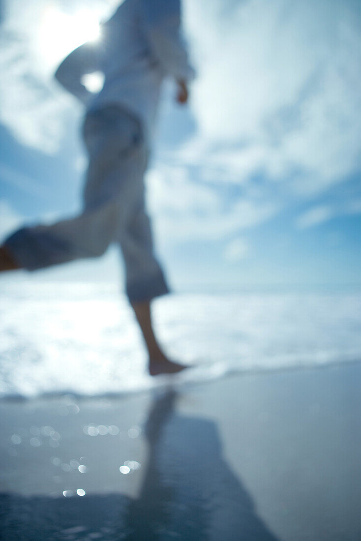 Man running at the beach, cropped view, defocused