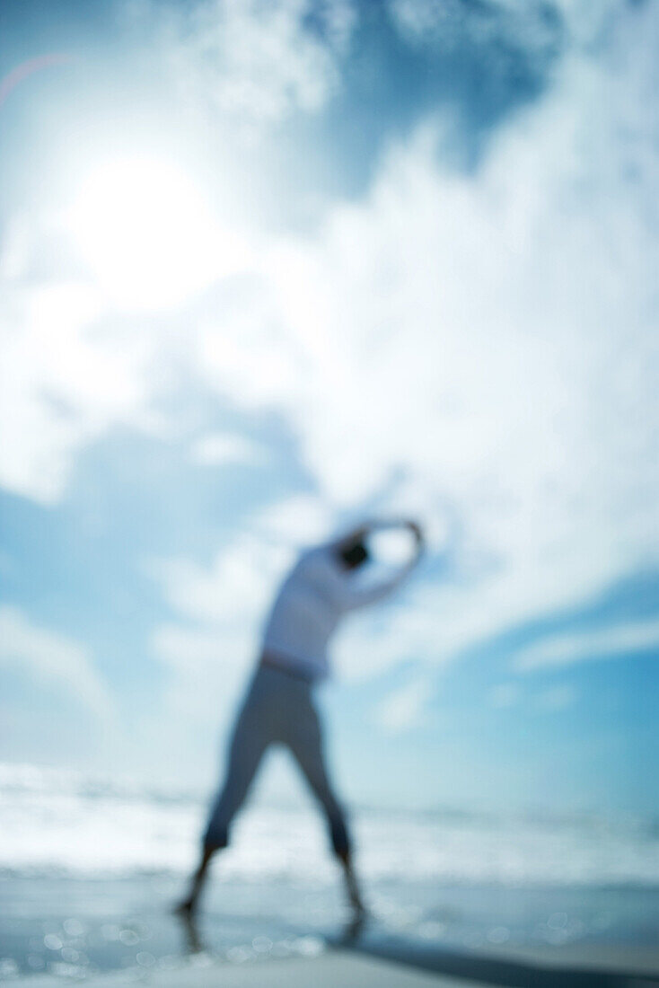 Person standing at the beach, arms raised, rear view, defocused