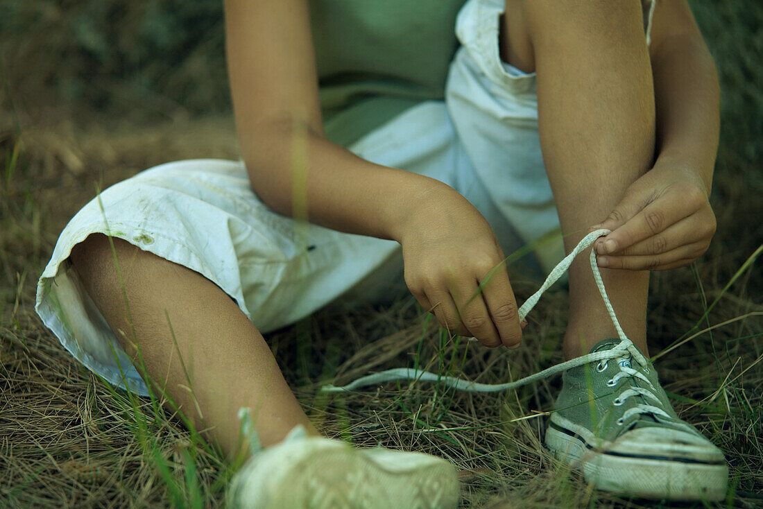 Little boy sitting on the ground, tying shoelaces, cropped view