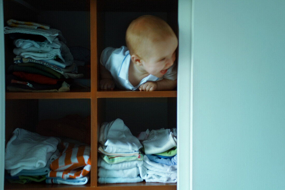 Baby boy peeking out of shelf, looking away