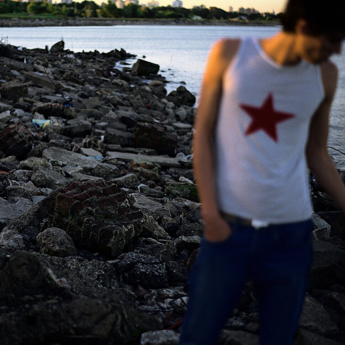 Young man standing on rocky shore, hand in pocket