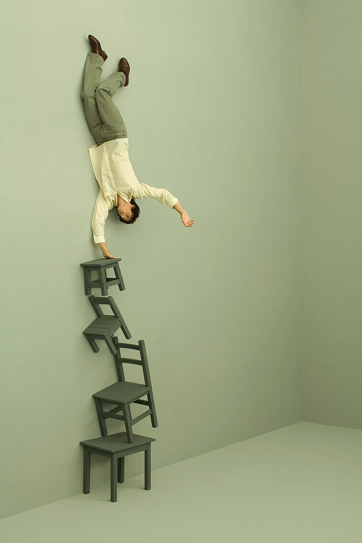 Man balancing on one hand on tall stack of chairs