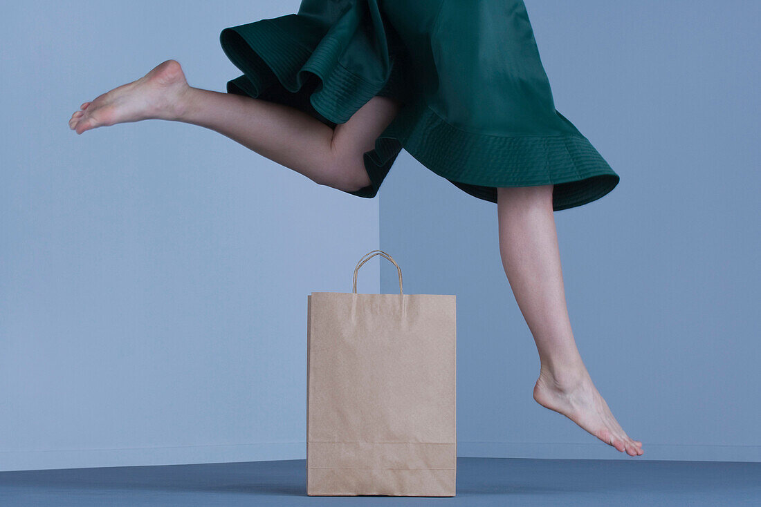 Female jumping over shopping bag, low section