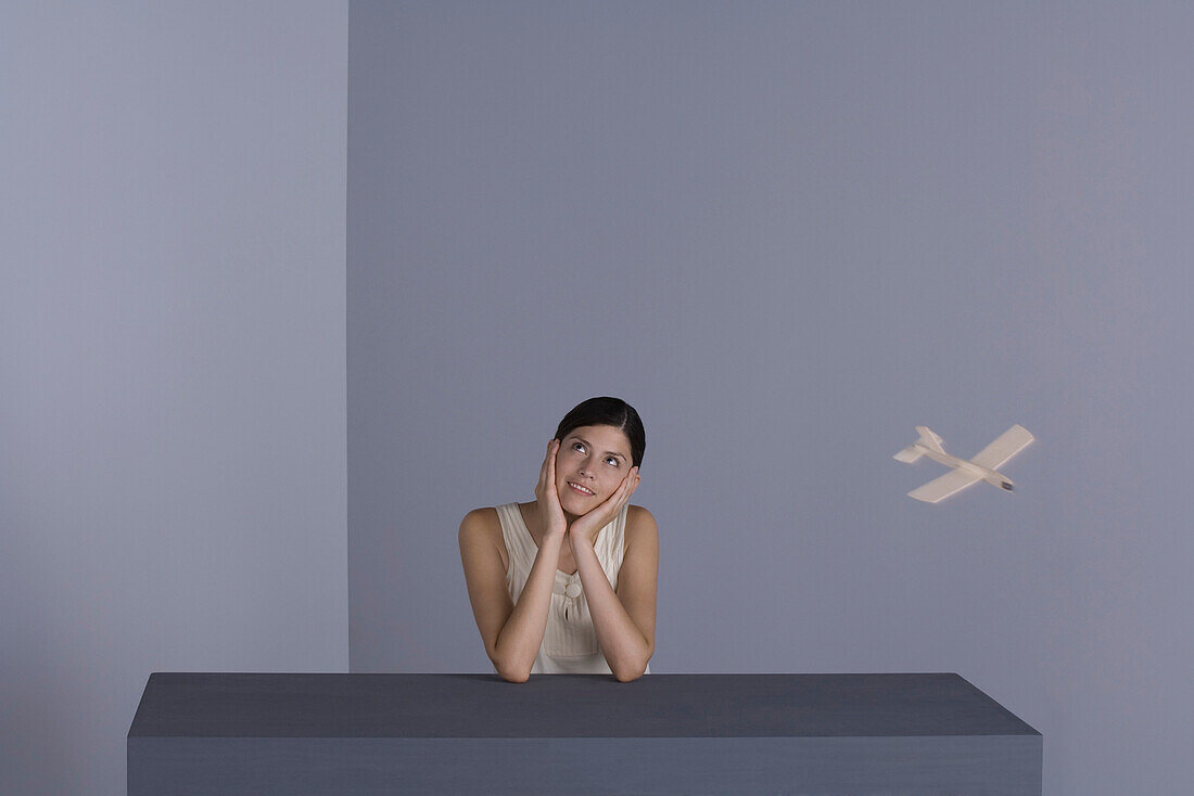 Woman holding head and smiling, toy airplane flying around her