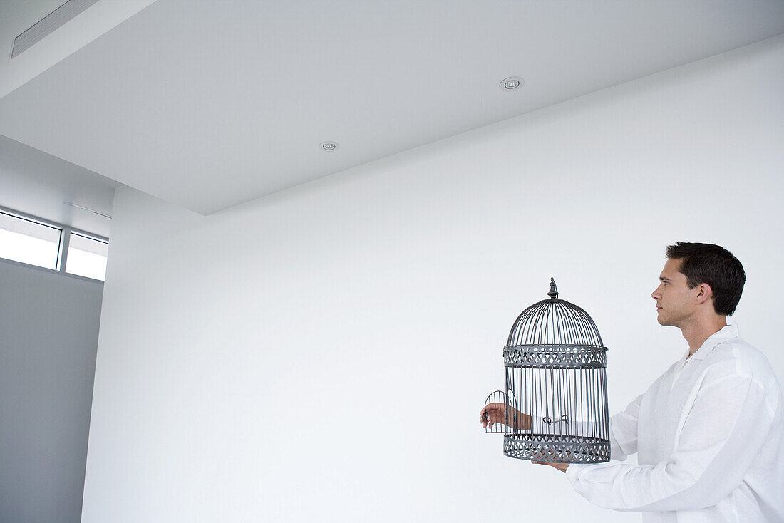 Man holding empty bird cage with open door, side view